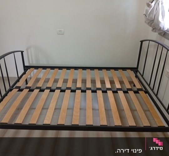 מיטה עם מסגרת מתכת ולוחות עץ בחדר ריק